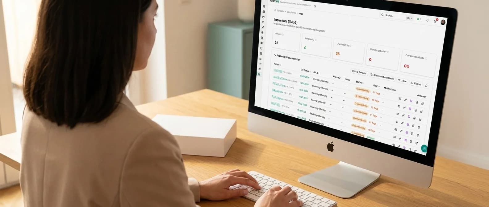 Praxismitarbeiterin am 27-Zoll-iMac mit dem AesthOS-Implantatregister-Dashboard — KPI-Kacheln und Liste offener iRegG-Meldungen mit Status Unvollständig und Restfristen, daneben eine neutrale Implantat-Schachtel